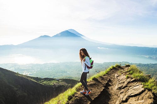 A scenic view from the Mount Batur hike at sunrise, showcasing the volcanic peak surrounded by lush greenery and a vibrant sky with hues of orange and pink.