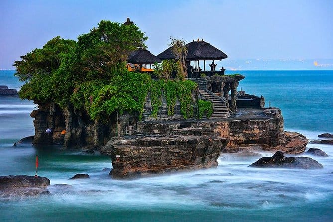 Scenic view of Tanah Lot Temple in Bali, perched on a rocky coastline with waves crashing below, a popular cultural and spiritual tourist destination.