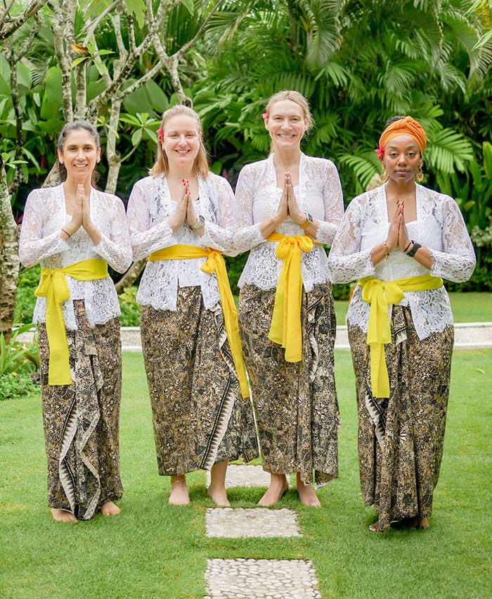Women enjoying a serene moment during a Bali retreat tour at Tanah Lot temple, with ocean views and cultural beauty in the background