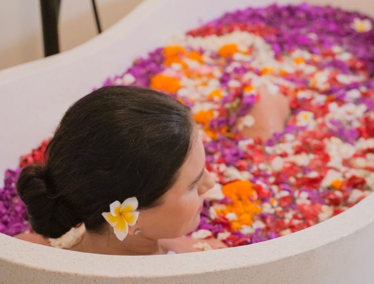 Woman relaxing in a flower bath at a spa, surrounded by vibrant petals.