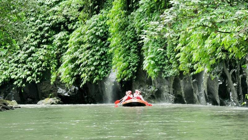 Adventurers navigating the rushing rapids of a tropical river in Ubud, Bali, surrounded by lush green jungle